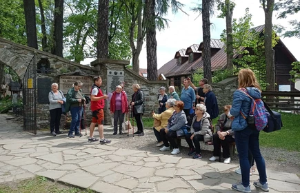 Grupa Seniorów stojąca przed wejściem na Najstarszy Cmenatrz w Zakopanem słuchających historii opowiadanej przez przewodnika